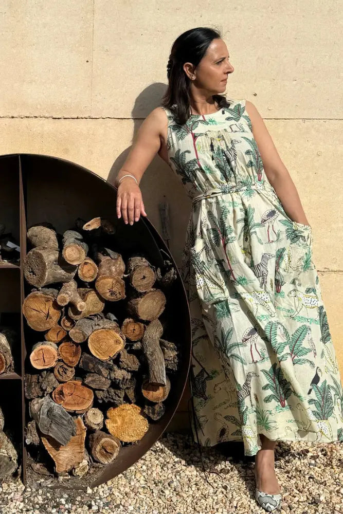 Tina in the green Ripple Maxi dress leaning against a stone wall next to a firewood holder.